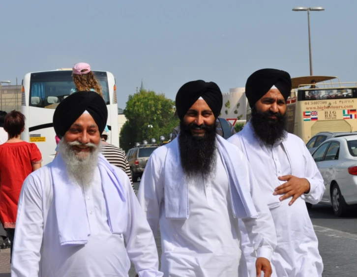 three men wearing turbans walk through a busy street