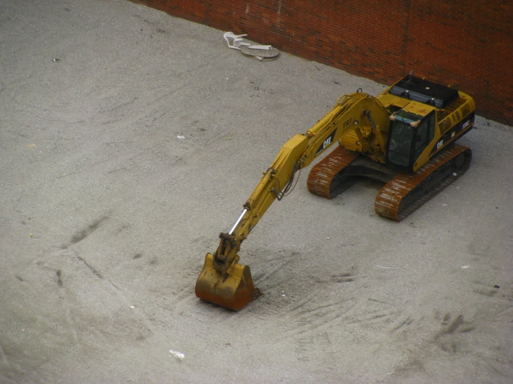 a small, yellow construction vehicle sits on concrete with brick walls behind it