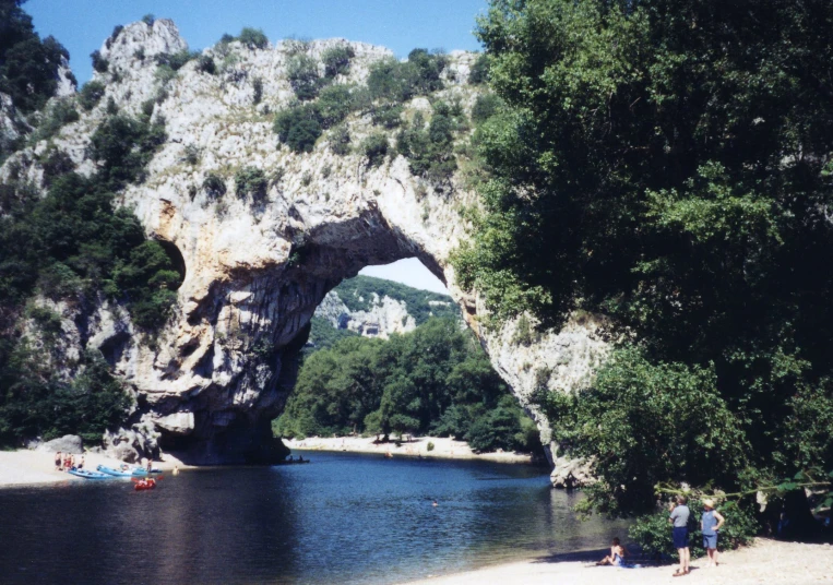 a stone arch on a beach surrounded by a forest