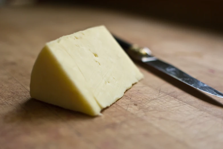 a piece of cheese sitting next to a knife on a table