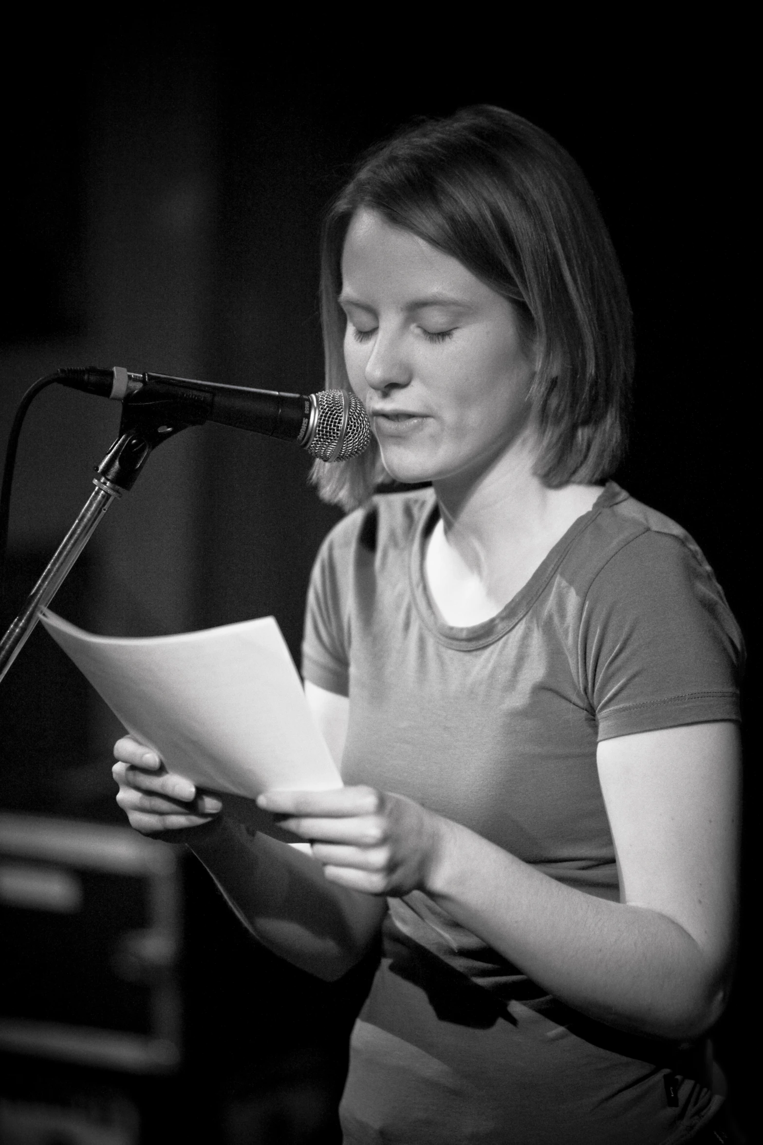 a woman reading a newspaper while standing next to a microphone