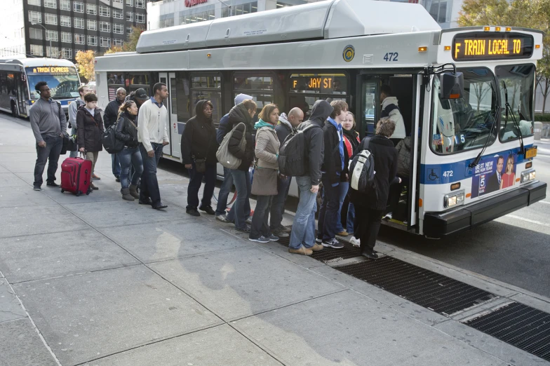 passengers are lined up at a bus stop to get on and off the bus