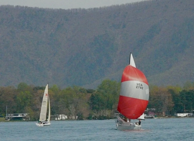 two sailboats on a lake with trees in the background