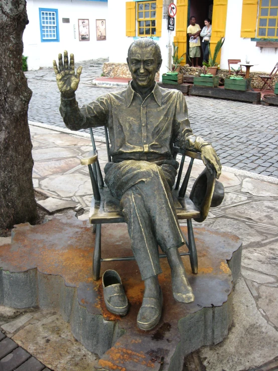 a statue sitting in a rocking chair on the sidewalk