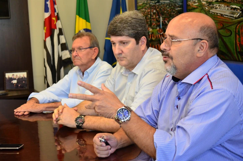 a group of men in blue shirts sitting around a wooden table