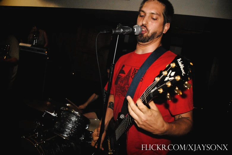 a man that is standing with his guitar near some drums