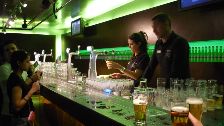 four people standing at the bar preparing glasses of beers