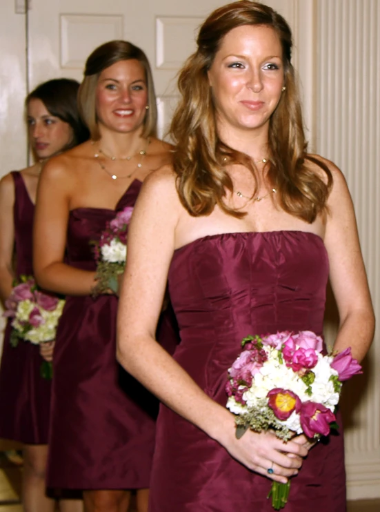 three women wearing dark purple bridesmaid gowns and holding flowers