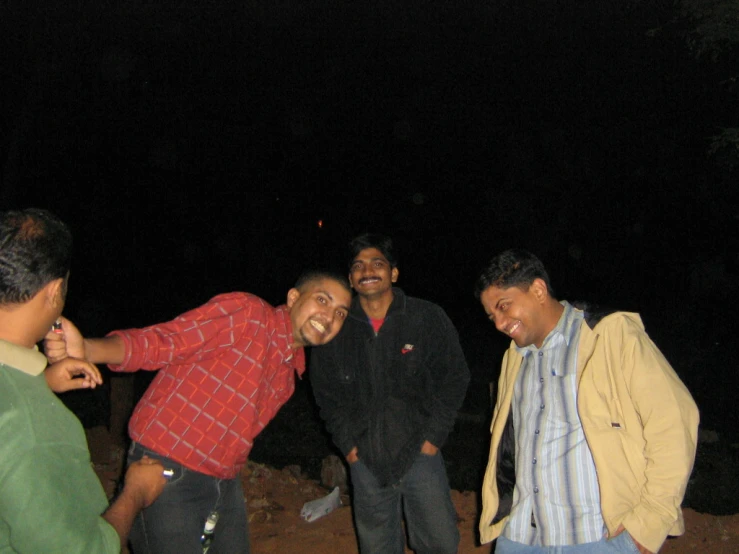 four men are laughing and having a conversation in the dark