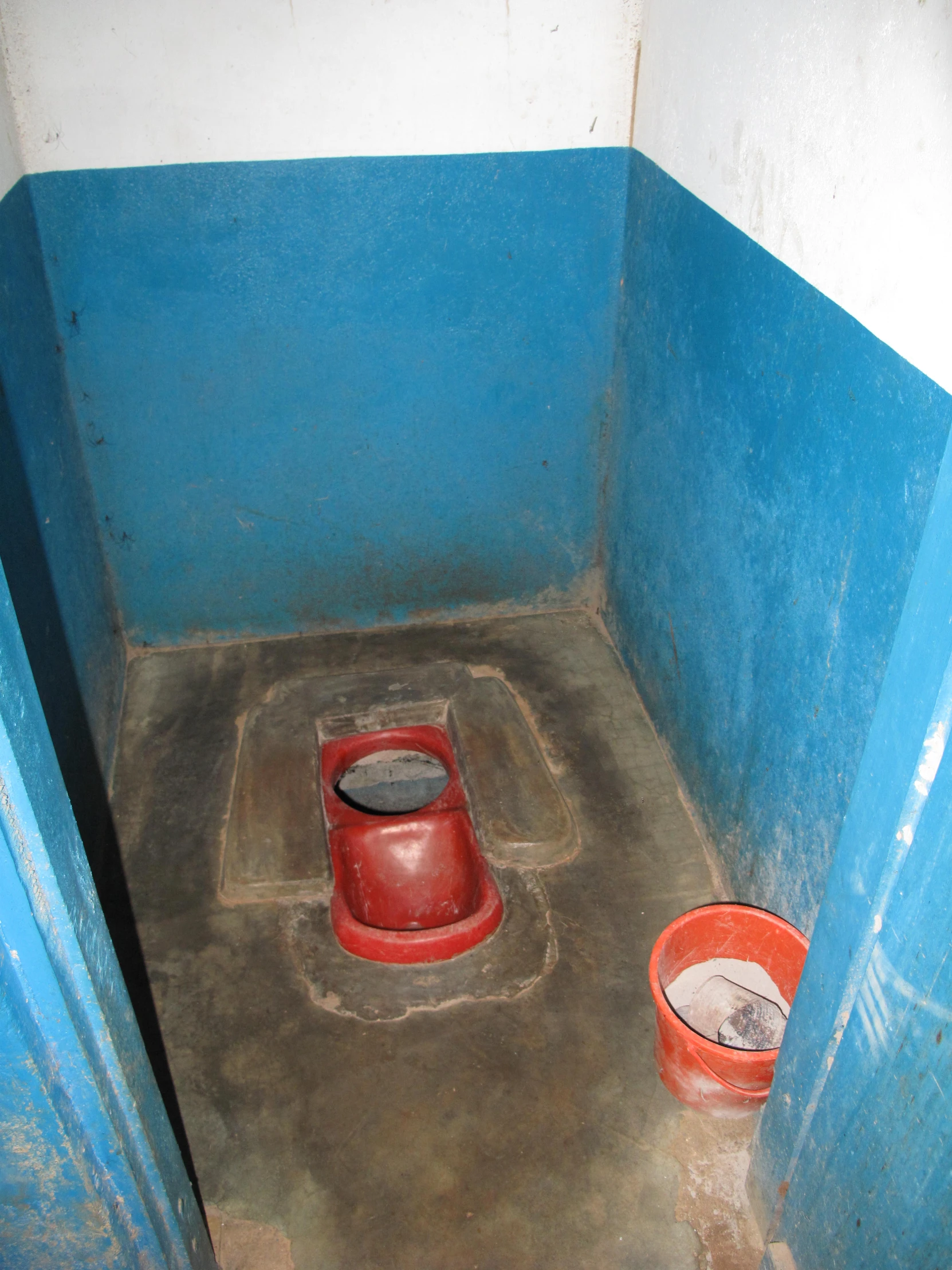 an open small red toilet sitting in a bathroom stall