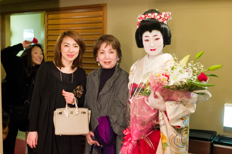 two women smile and pose beside a statue of geisha