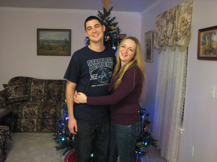 two people posing for a picture next to the christmas tree