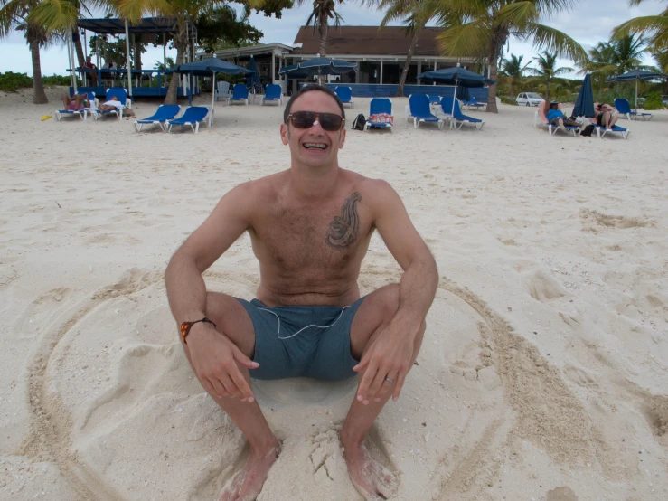 a guy is smiling and making faces while sitting on the beach