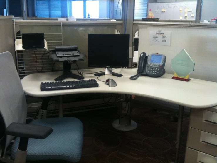 an office desk with a telephone, computer monitor, keyboard, and a chair