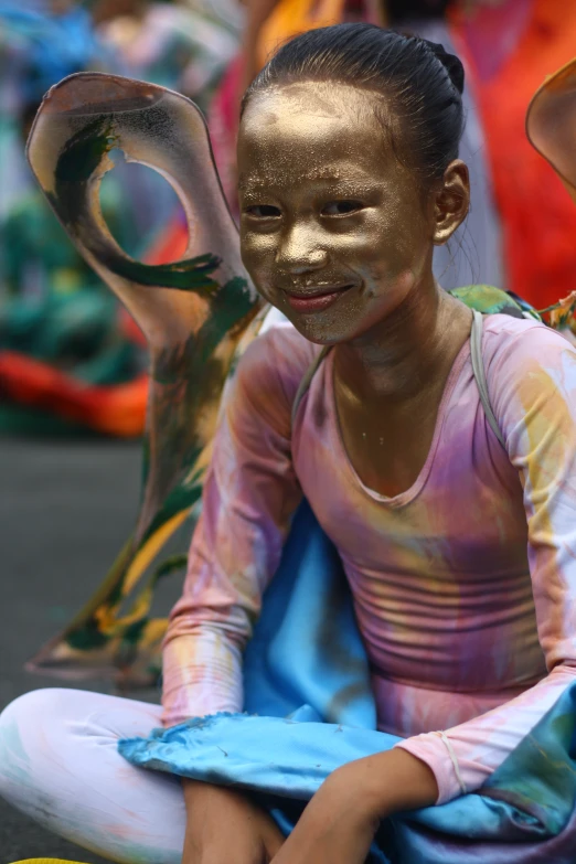 a girl with paint all over her face sits on the ground
