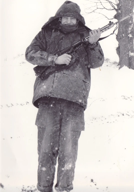 the man is carrying his rifle while standing in snow