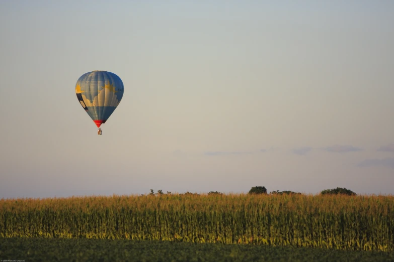 a large blue  air balloon flying over a dry grass field