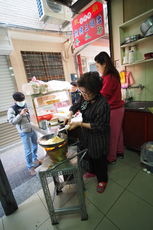 a woman in a black and white striped shirt cooking food in an open air kitchen