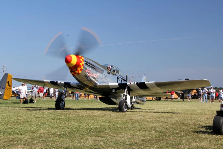 a small yellow and black airplane on grass with other people