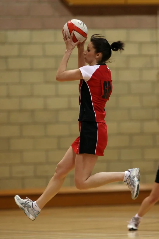 a girl in red and black uniform jumping up to get a basketball