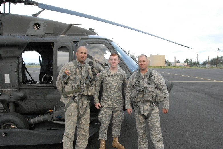 three men in camouflage uniforms standing next to a helicopter