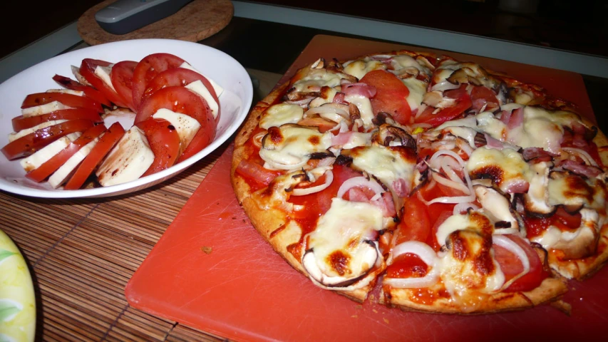 sliced tomatoes on a pizza sitting next to a bowl of onions
