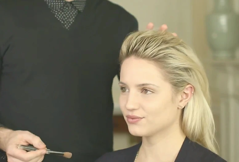 a blond woman getting her make - up done while a man looks on