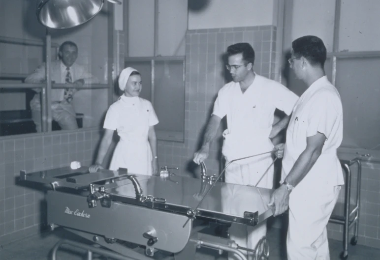 a group of three men in white lab coats in a room with tiled walls and gray flooring