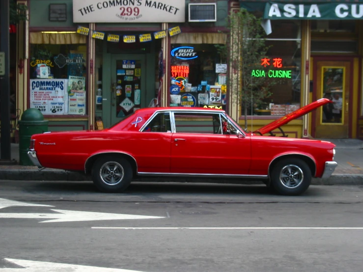 the red vintage car is parked outside the shops