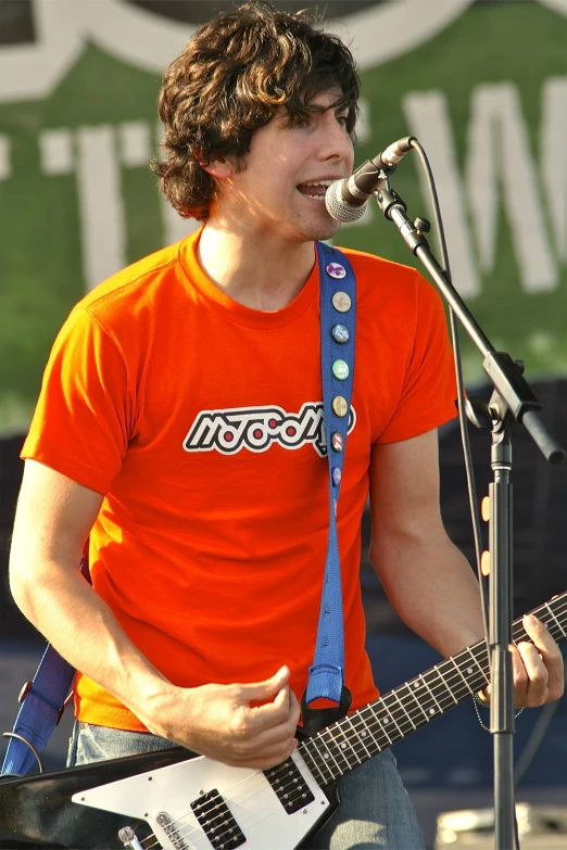 a man wearing an orange shirt and blue band aids a guitar