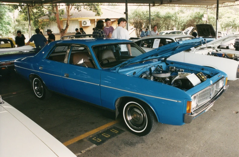 a blue muscle car with its hood open and people around it