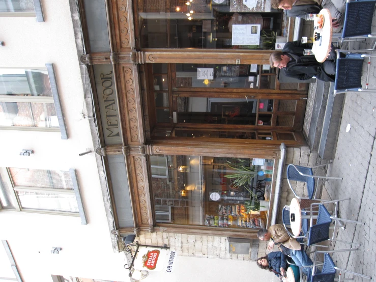 people sitting outside in outdoor restaurant chairs in front of building