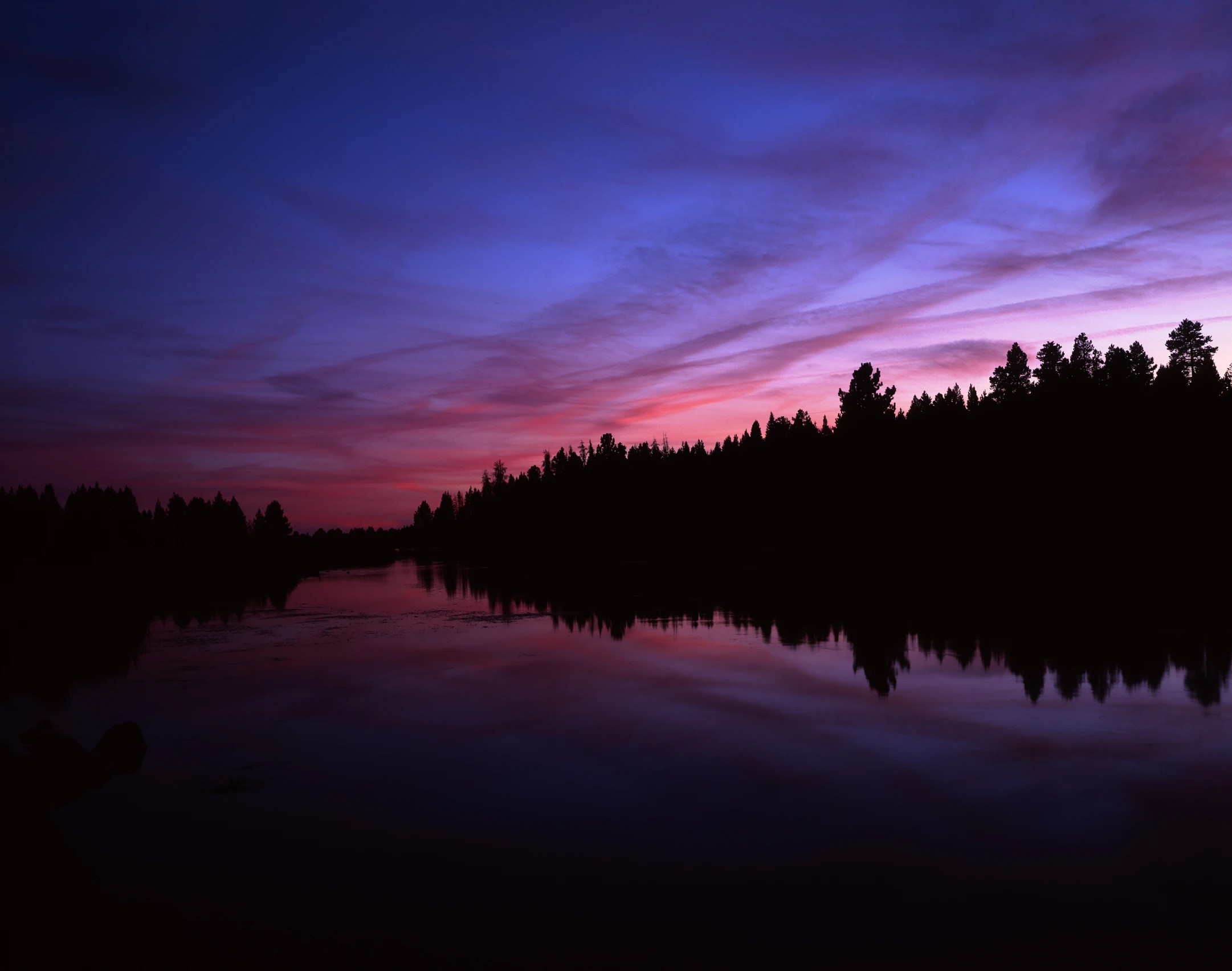 this is a purple sky at sunset and it reflects the reflection of a forested area