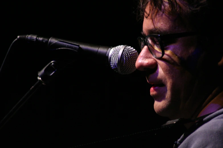 man wearing eyeglasses singing into a microphone