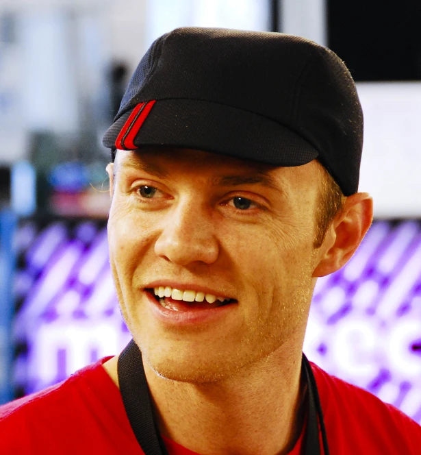 a smiling man wearing a red shirt and black hat