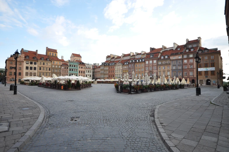 an empty paved city plaza has many tables with umbrellas on it