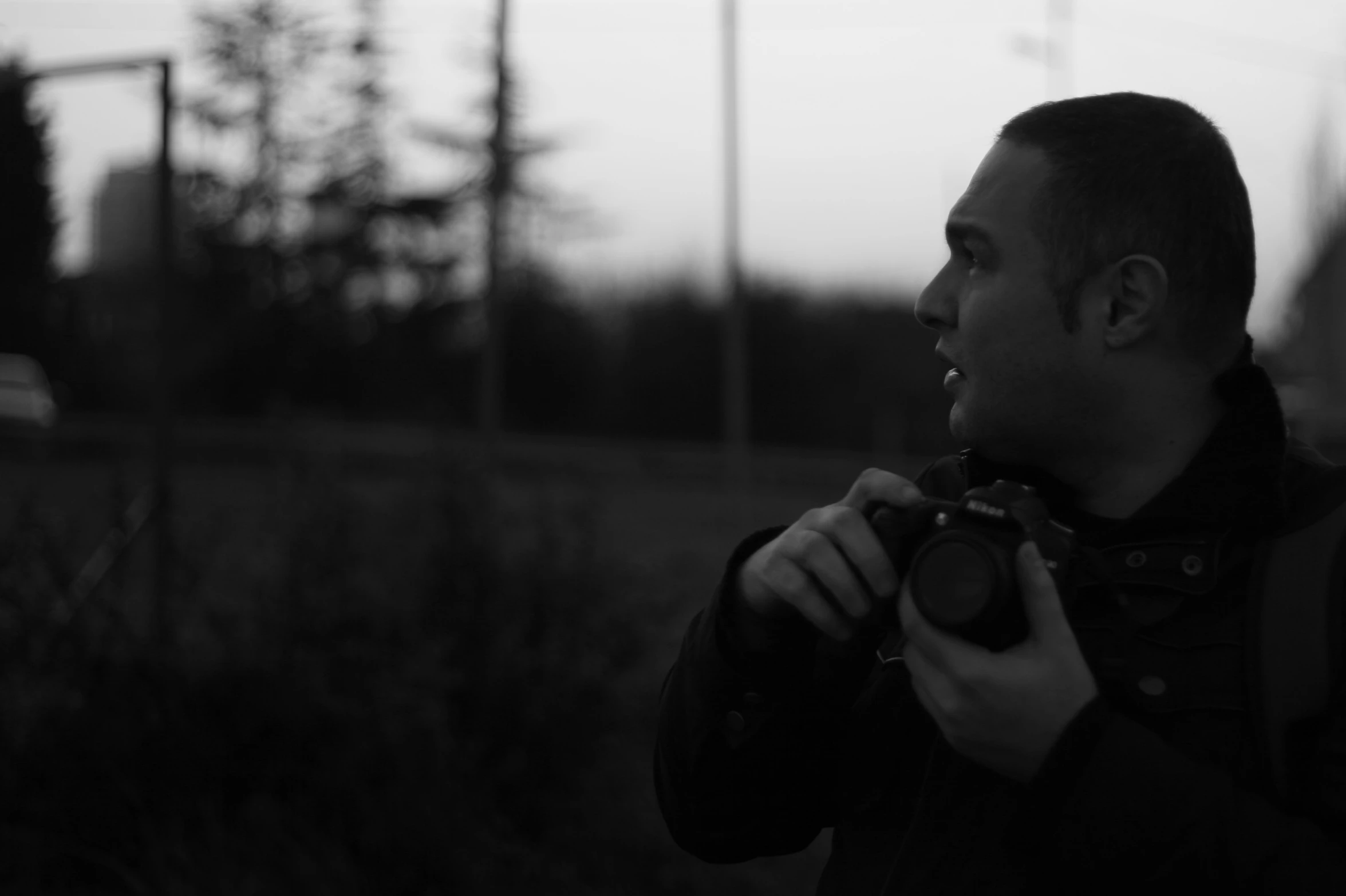 a man in black jacket holding camera by some grass