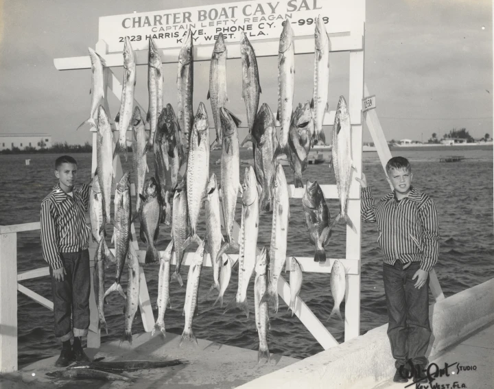 two boys standing in front of a sign with fish hanging from it