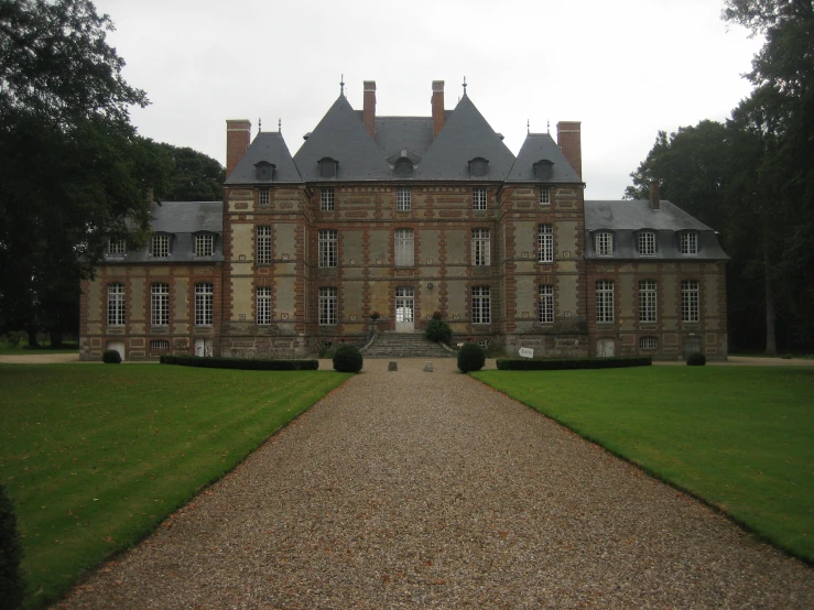 an old, red brick building with tall towers stands in a large yard