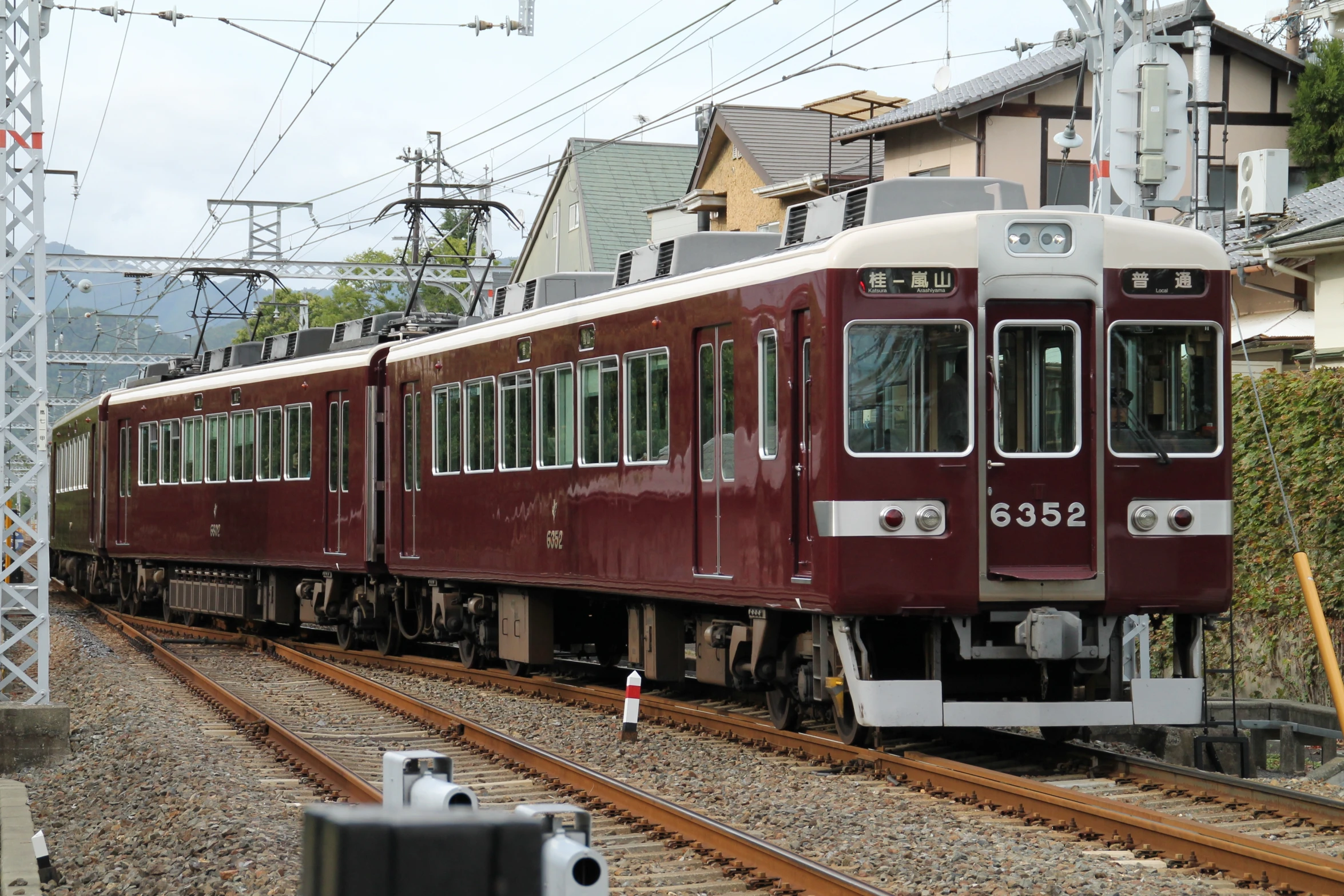 a maroon train traveling past a couple of houses