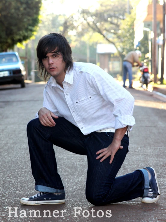 a man crouches on the ground near a skateboard