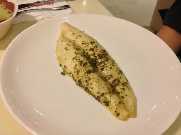 cooked fish on a white plate with small dish