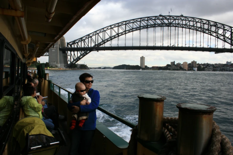 a man holding a child on a boat next to a bridge