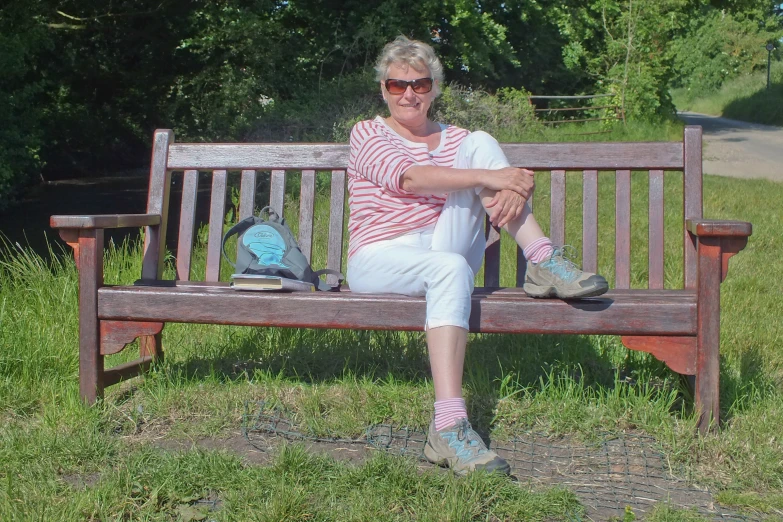 an older woman wearing glasses and sitting on a bench in a park