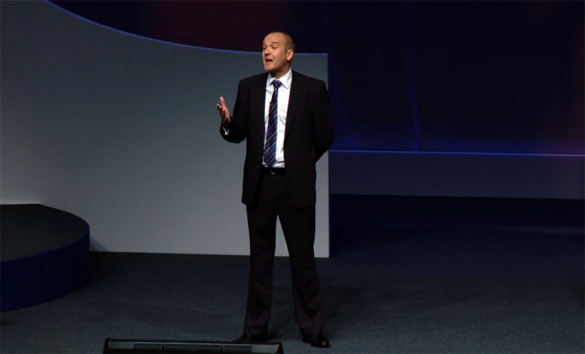 a man in a suit stands on stage and speaks