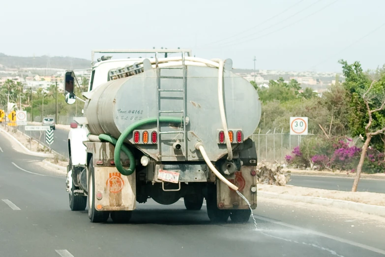 man washing off the water from a tank that is attached to the back of a truck