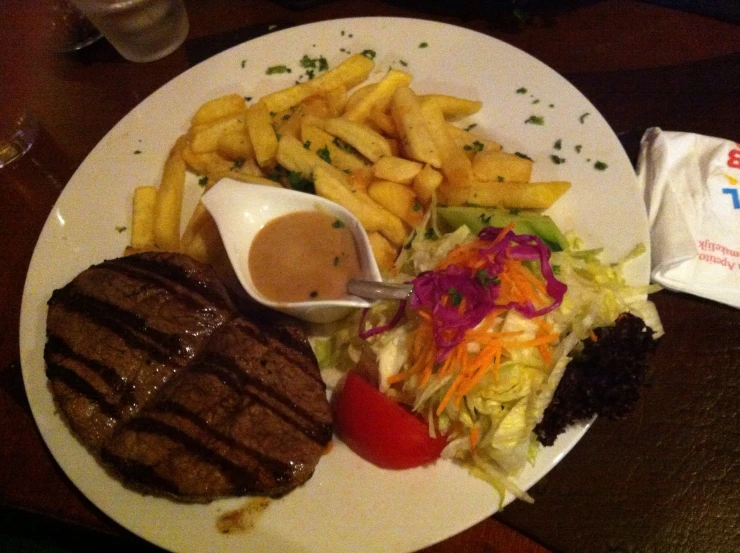 steak, fries, vegetables and a gravy sit on a plate
