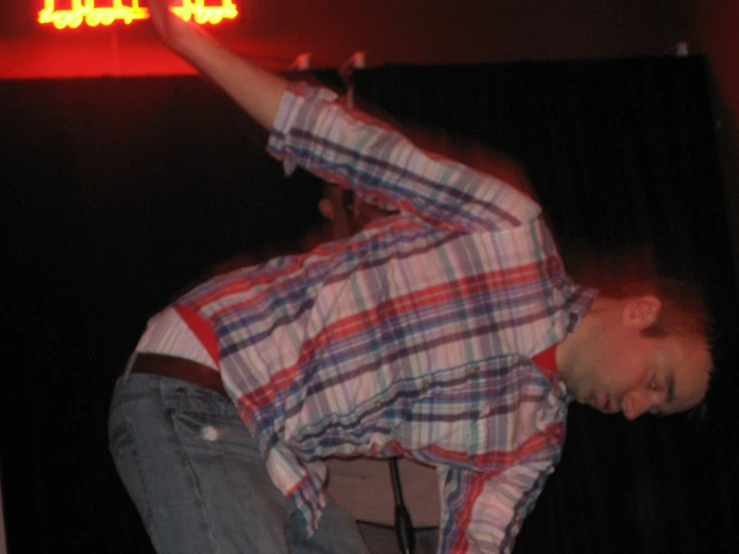 a guy leaning on the edge of a table in front of a neon sign