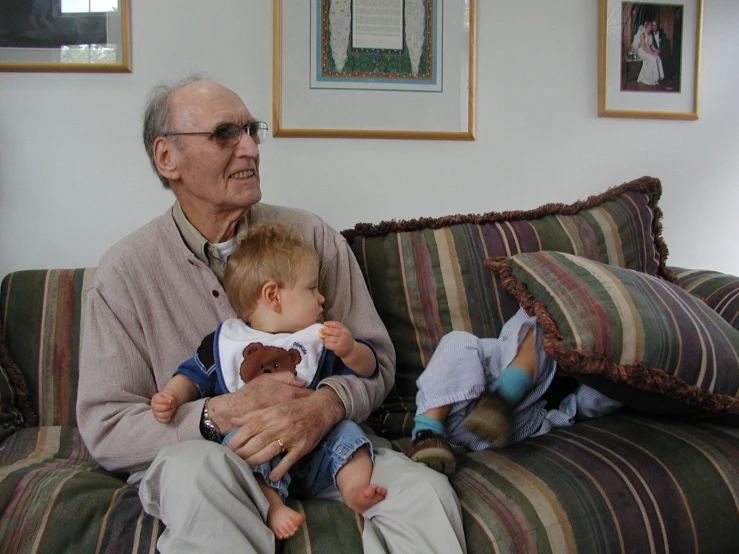 an elderly man holds his two children on the sofa