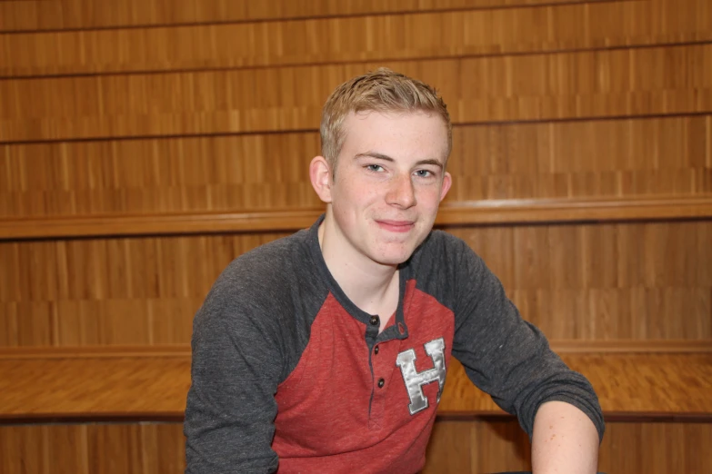 a man in a red shirt smiling near a book shelf